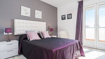 Une chambre à coucher avec un grand lit, deux tables de chevet, une commode, une chaise et une vue sur l’extérieur, accessible par une porte coulissante.