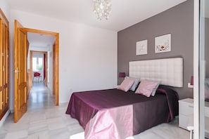 Un dormitorio con cama, mesitas de noche, un armario y un pasillo que conduce a otra habitación.