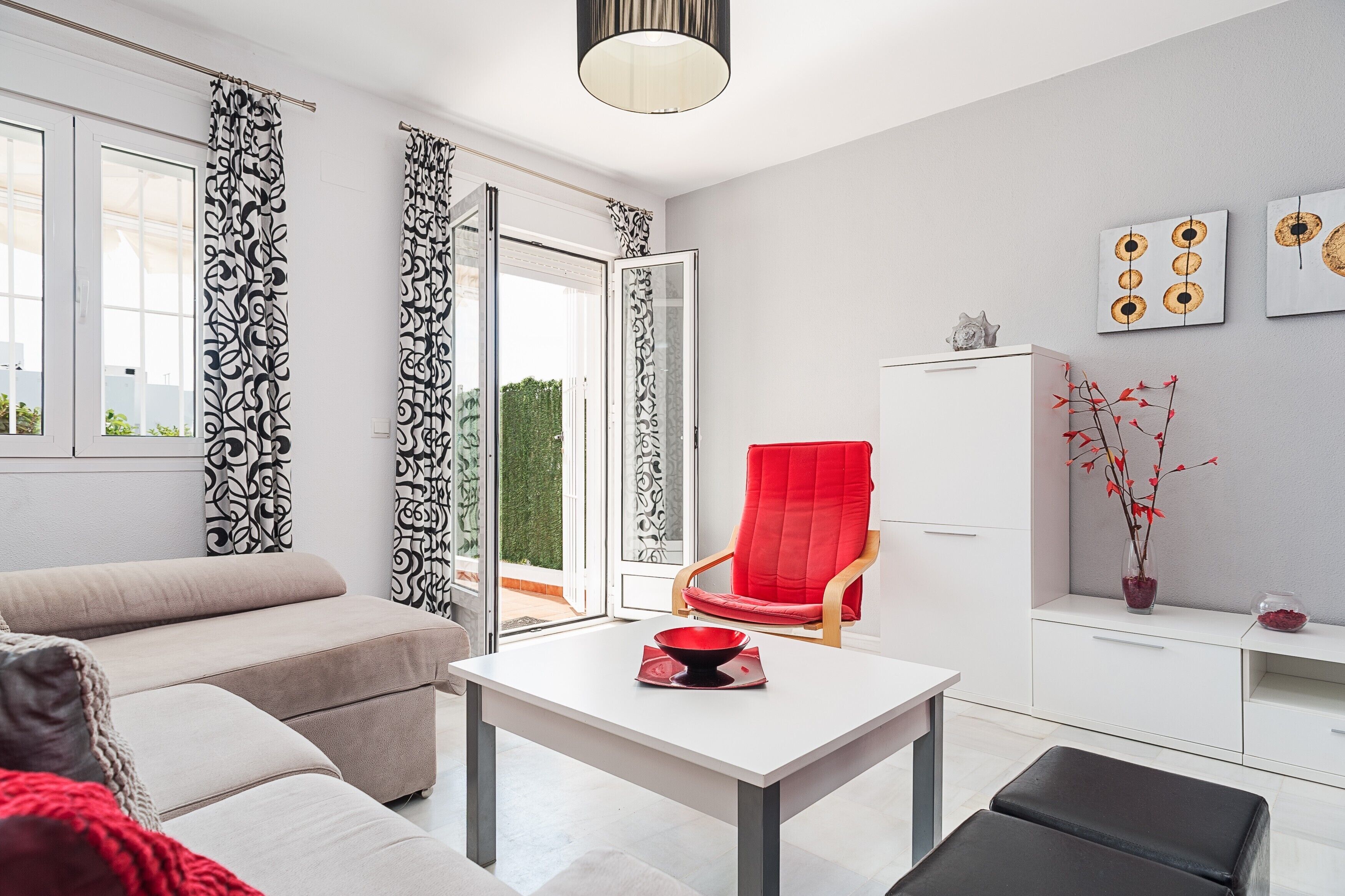 Un salon moderne avec un canapé, un fauteuil rouge, une table blanche et un meuble.