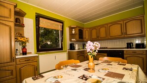 Una cocina con armarios de madera, una mesa de comedor con mantel y un ventanal con persianas.