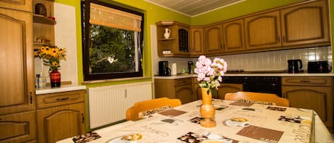 A kitchen with wooden cabinets, a dining table with a tablecloth, and a window with blinds.