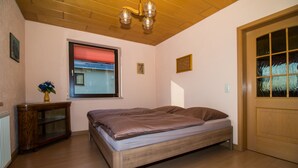 Un dormitorio con una cama y un aparador de madera, una ventana con persiana roja y una puerta con paneles de vidrio.