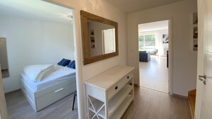 Ein Schlafzimmer mit einem Bett, einem Nachttisch, einem Spiegel und Blick in den Wohnbereich.