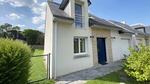 Ein modernes, zweistöckiges Haus mit Natursteinfassade, einer dunkelblauen Tür und einem kleinen Vorgarten.