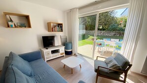 Ein Wohnzimmer mit einer Couch, einem Couchtisch, einer TV-Konsole und einer Glastür, die zu einer Außenpatio führt.