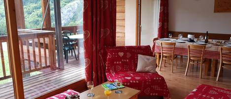 Una habitación acogedora con una terraza de madera, un comedor con una mesa lista para dos personas y un sofá rojo estampado.