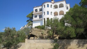 A white building with multiple balconies and arched windows, situated on a hillside with surrounding vegetation. - The Calm And The View For 4 to 5 People (Rosas)