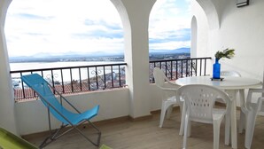 A balcony with a view of a cityscape, white chairs, a table, and a blue chair. - The Calm And The View For 4 to 5 People (Rosas)