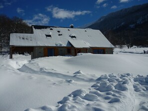 Un edificio cubierto de nieve con techo inclinado, muros de piedra y puertas de madera.