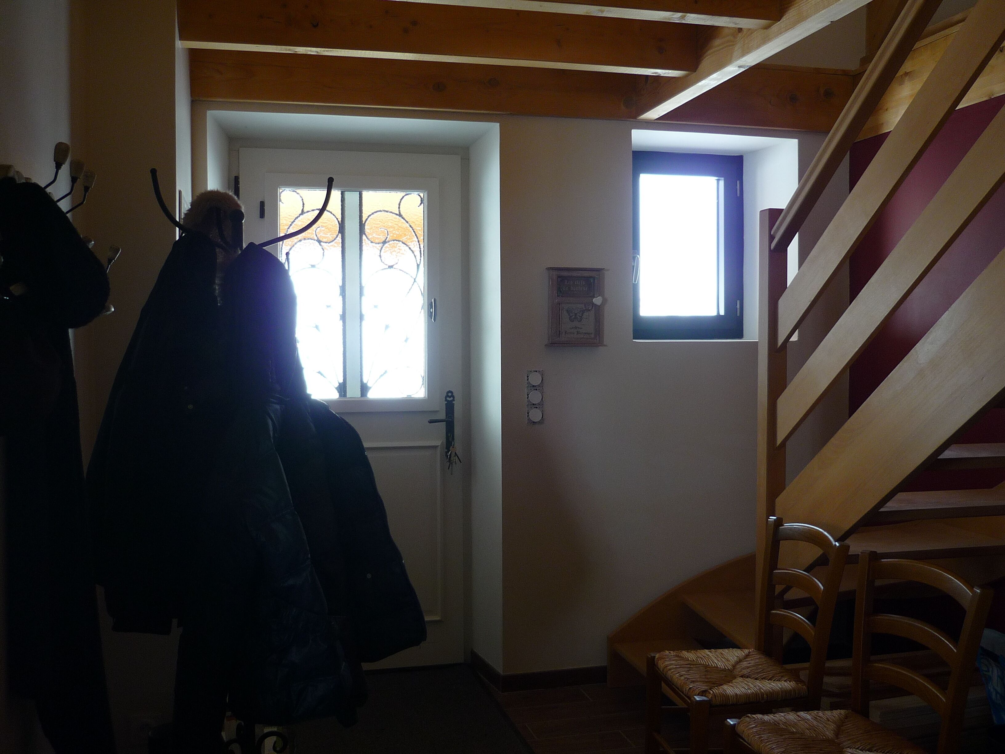 Eine Treppe mit Holzgeländern führt zu einer oberen Etage. Im Hintergrund ist eine Tür mit einem Fenster zu sehen.