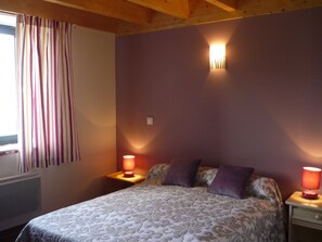 Un dormitorio con cama, dos mesitas de noche, una ventana con cortinas y una lámpara de pared.