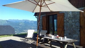 Un espace de restauration en plein air avec une table et des chaises, un parasol et une vue sur les montagnes en arrière-plan.