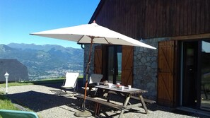 Zona de estar exterior con mesa y sillas bajo un paraguas grande, con vistas a un paisaje montañoso.