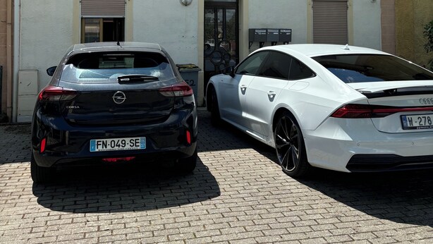 Zwei Autos vor einem Gebäude mit einem Ziegeldach und vielen Fenstern geparkt.