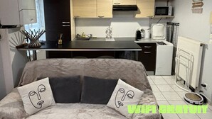 Eine moderne Küche mit einer zentralen Kochinsel, einer Mikrowelle und einem Kühlschrank. Ein Sofa mit gemusterten Kissen und eine Katzentoilette stehen auf dem Boden.