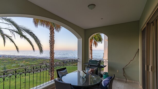 A balcony with a glass table and chairs, overlooking a grassy area and the sea. - Memorable revival unit (La Paz)