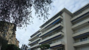 A multi-story building with balconies, a central entrance, and surrounding greenery. - Studio sea view, wifi, spacious + balcony, near beach and shops (Menton)