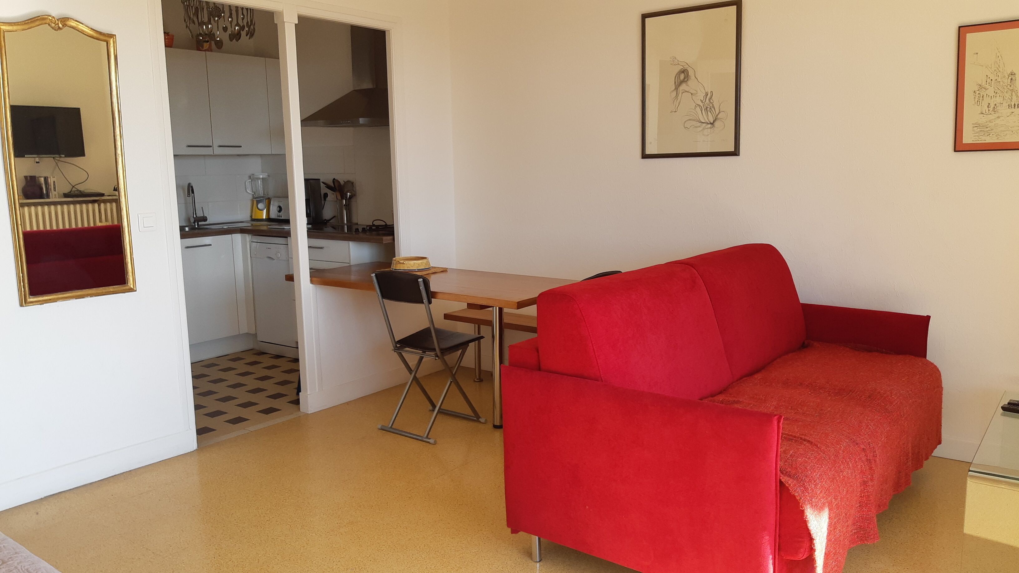 A compact living space with a red sofa, a dining table, and a kitchen area.