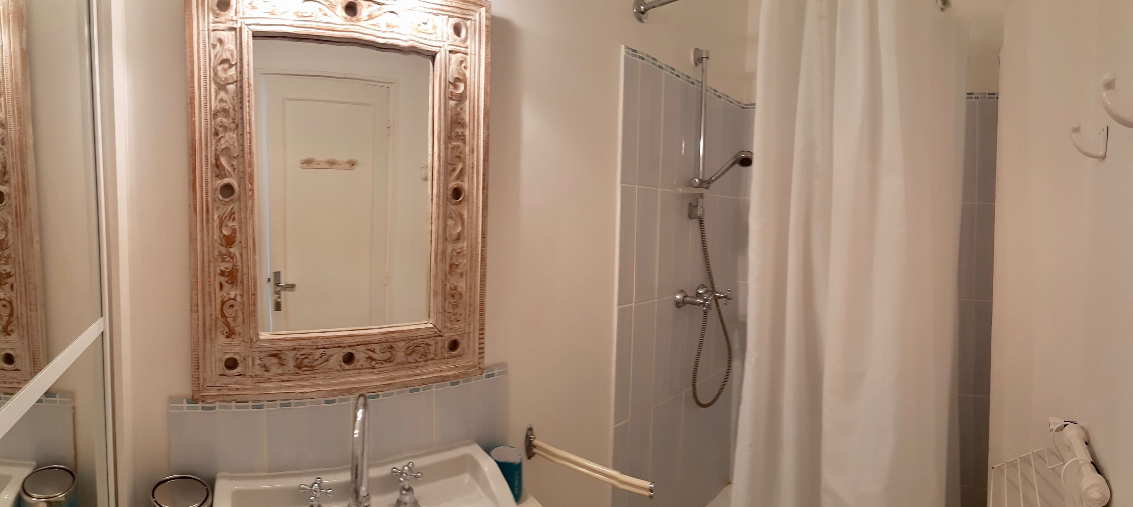 Une salle de bain dotée d’un grand miroir décoratif, d’une douche avec un pommeau de douche amovible et d’une baignoire blanche.