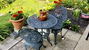 Une terrasse agrémentée de deux tables et chaises en métal ouvragé, entourée de plantes en pot et d’une clôture en bois.