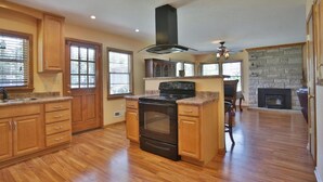 Une cuisine spacieuse avec des meubles en bois, un îlot central, une cuisinière et une cheminée en pierre.