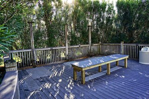 Een houten terras met een metalen tafel en bank, omgeven door een houten hek en weelderige beplanting.