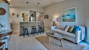 Una cocina moderna con una isla central, taburetes de bar, iluminación colgante y un comedor con mesa de vidrio.