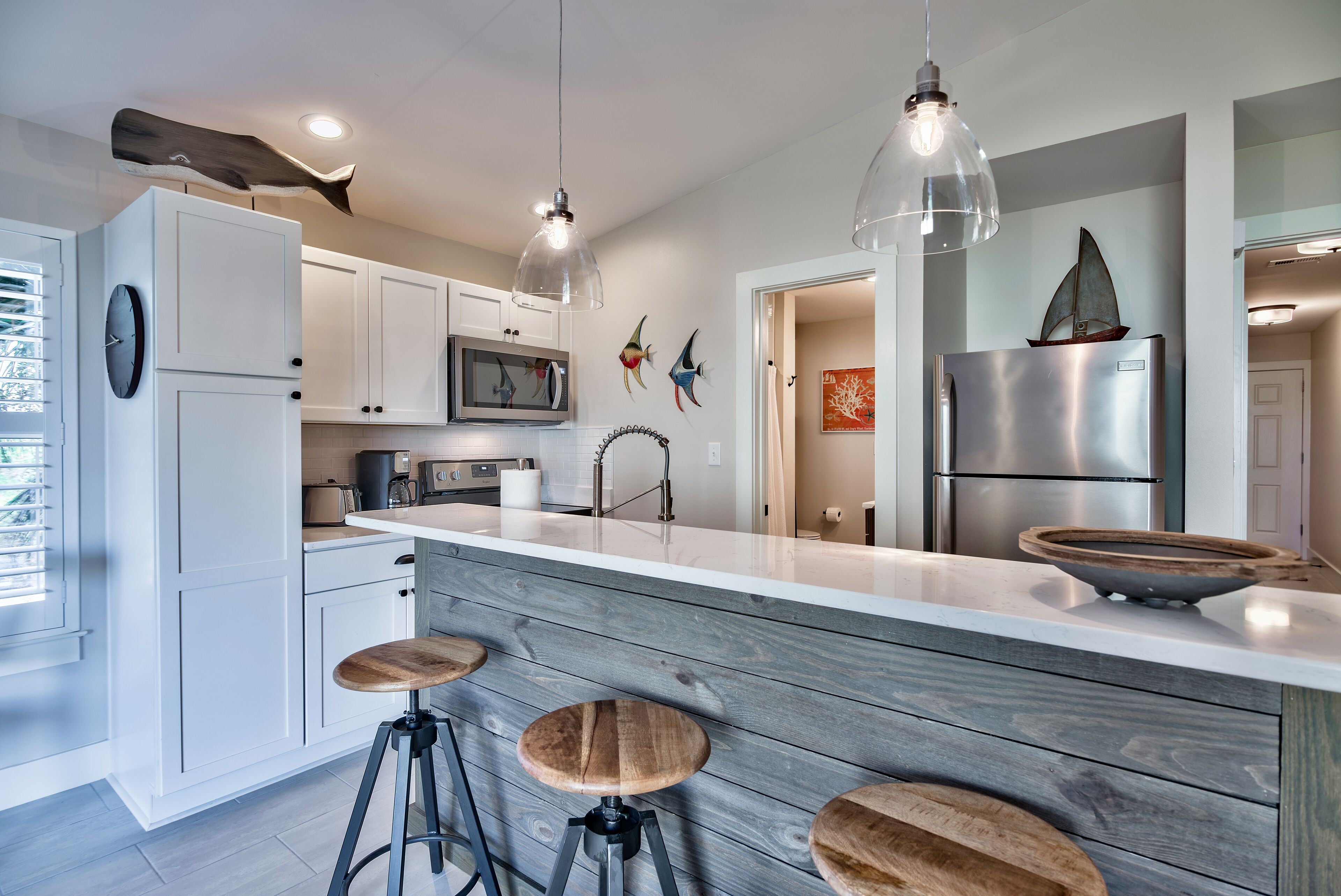 A modern kitchen with white cabinets, a wooden island with stools, a stainless steel refrigerator, and decorative wall art.