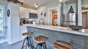 Una cocina moderna con armarios blancos, una isla de madera con taburetes, un refrigerador de acero inoxidable y decoración en la pared.