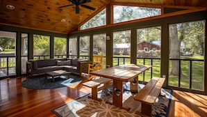 Un espace intérieur vaste et lumineux, avec un plafond en bois, de grandes fenêtres, une table en bois, un canapé et un banc.
