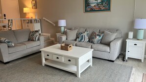 A living room with a grey sofa, a white coffee table, and a painting of a beach scene on the wall.
