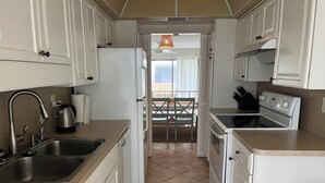 A compact kitchen with white cabinets, a stainless steel sink, a kettle, and a stove.