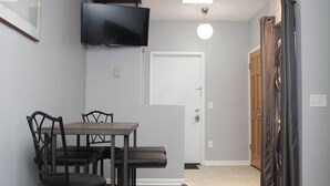 Un coin repas avec une table et des chaises, un téléviseur fixé au mur, une porte et un rideau à motifs.