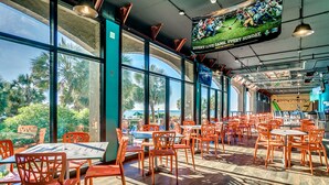 A spacious restaurant with large windows, orange chairs, and a view of palm trees. - Oceanfront Suite w/Amazing View + Official On-Site Rental Privileges (North Myrtle Beach)