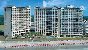 A beachfront hotel with multiple floors, a pool, and a beach area with umbrellas. - Oceanfront Suite w/Amazing View + Official On-Site Rental Privileges (North Myrtle Beach)