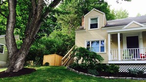 A two-story house with a front porch, a wooden shed, and a large tree in the yard.