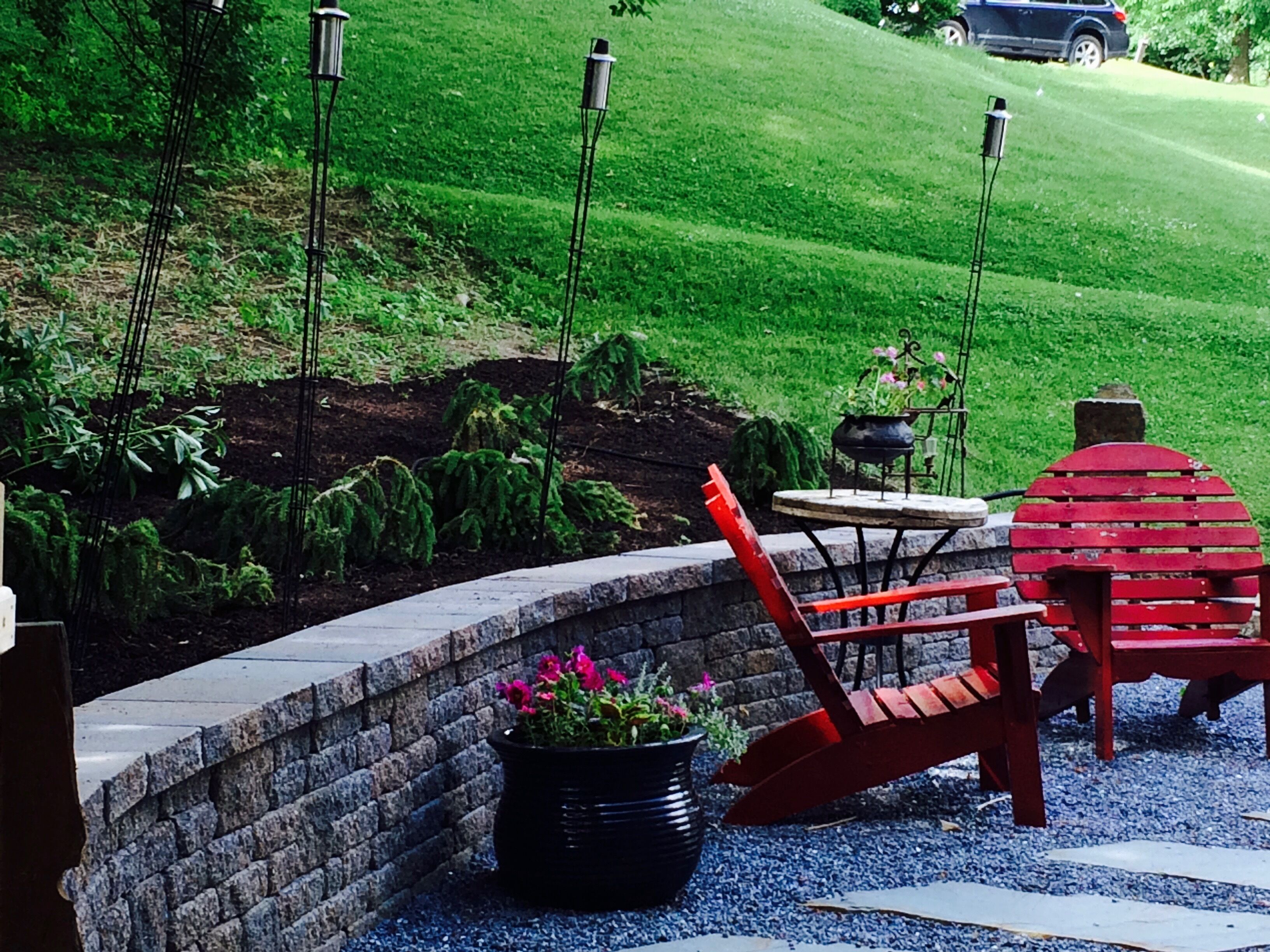 Un espace patio agrémenté d’un mur en briques, d’une chaise rouge, d’une table et d’une plante en pot.