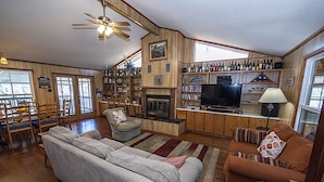 Una sala de estar acogedora con chimenea, televisor y una estantería llena de libros y objetos decorativos.