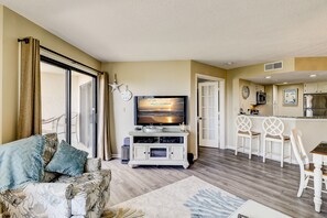 A living room with a sofa, TV, and a kitchen area with bar stools.