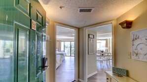 Un pasillo de hotel con una puerta verde, un comedor con mesa y sillas, y un cuadro en la pared.