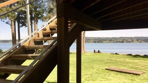 A wooden staircase leading to a covered area with a view of a lake and a grassy area with a wooden deck.