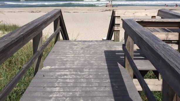 A wooden boardwalk leading to a beach with a clear view of the ocean.
