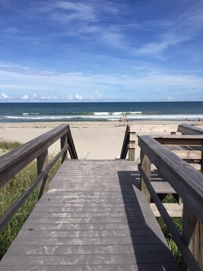 Eine Holzpromenade, die zu einem Strand führt, mit freiem Blick auf den Ozean.