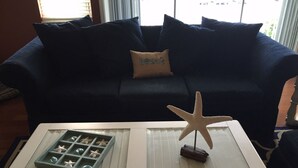 A living room with a dark blue sofa, a glass coffee table with a starfish decoration, a remote control, and a decorative tray with starfish.