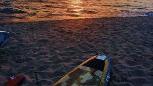Une plage avec une planche de surf et un kayak, et le soleil se couchant sur l’océan.