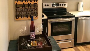 Une cuisine avec des meubles de couleur sombre, un four à micro-ondes en acier inoxydable, un four et un plateau contenant des verres et des bouteilles de vin.