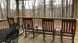 Eine Holzterrasse mit Tisch und vier Schaukelstühlen, mit Blick auf eine bewaldete Landschaft.