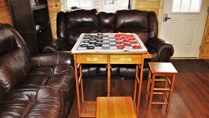 Ein Wohnzimmer mit einer braunen Ledersofa, einem Holztisch mit Schachbrett und einem kleinen Holzschemel.