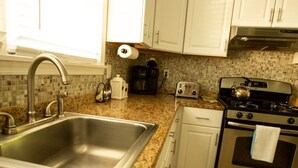 A kitchen with white cabinets, a stainless steel sink, a coffee maker, a toaster, and an oven. - 1st Class Rentals - Munson Manor III at Murdock (Oneonta)