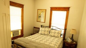 A bedroom with a bed, a nightstand, a lamp, and a window with blinds. - 1st Class Rentals - Munson Manor III at Murdock (Oneonta)